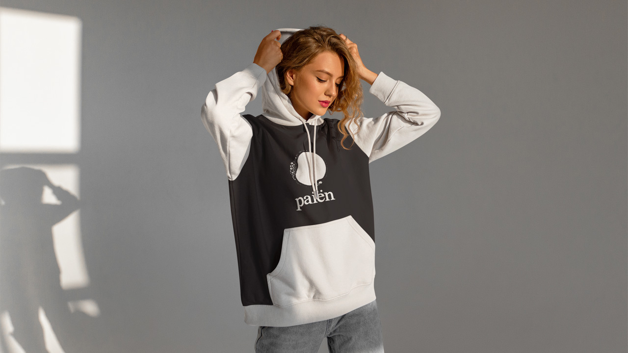 Merch. Photo of girl putting on a hoodie with the logo of Paiën on the front.